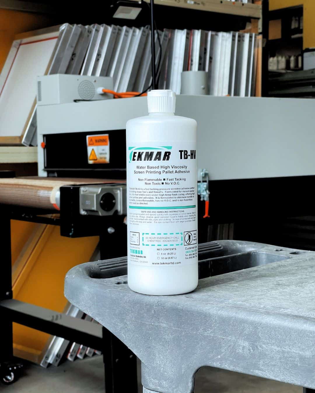 Tekmar TB-HV water-based high-viscosity pallet adhesive bottle with squeegee shown on a screenprinting platen. Clean, no-VOC adhesive exclusively stocked at Jones Brothers in Melbourne for professional screenprinters across Australia