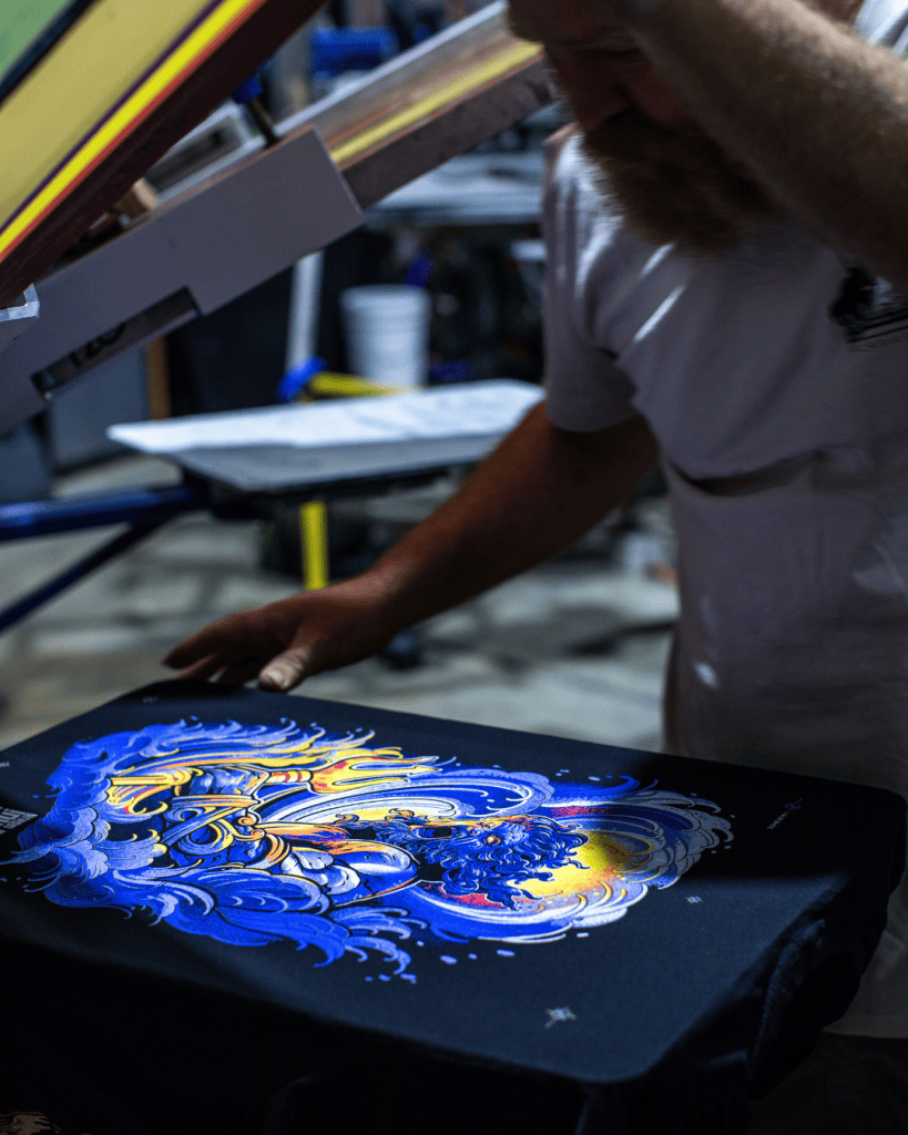 Hand-printed Project Poseidon artwork by Minnie Longstaff, screenprinted using Union Ink’s UPLC UNI MIX range supplied by Avient. Printed by BlackDog Ink on an M&R press, with garments supported by AS Colour. Materials supplied by Jones Brothers in Melbourne, Australia. Professional screenprinting process photo.