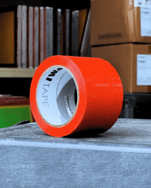 Bright orange packaging tape roll on a wooden surface in a warehouse.